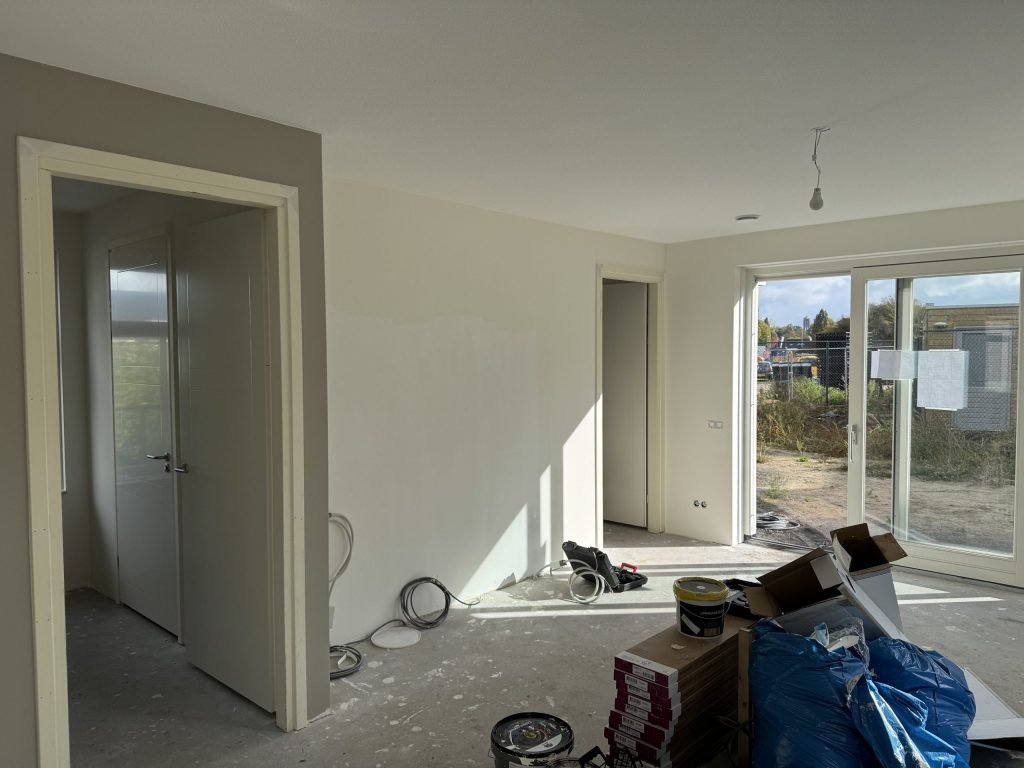 Nieuwbouwwoonkamer tijdens de afwerking, met emmers en materiaal op de vloer