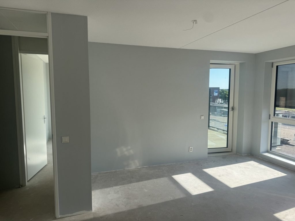 Nieuwbouwwoonkamer met egaal gesausde grijze wanden en zonlicht op de betonvloer