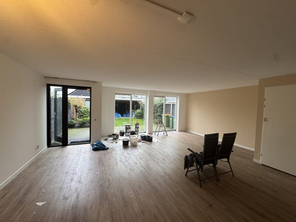 Ruime woonkamer met lichte wanden, een houten vloer en openslaande tuindeuren